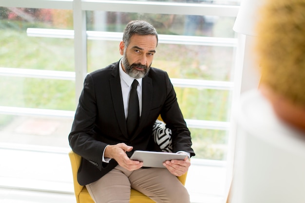 Foto knappe lachende volwassen zakenman met een tablet in het kantoor werken, lezen of iets zoeken