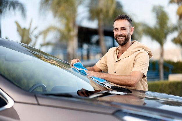 Knappe lachende werknemer schoonmaak auto met behulp van microvezeldoek. Auto wassen dienstverleningsconcept