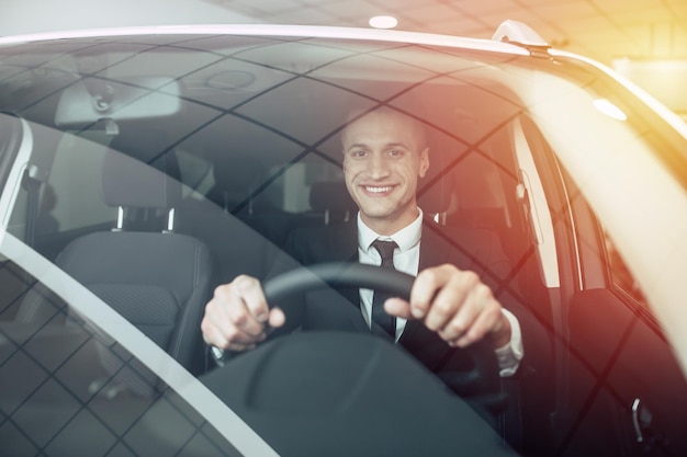 Knappe lachende zakenman die een auto bestuurt Man in fullsuit die auto koopt bij dealer