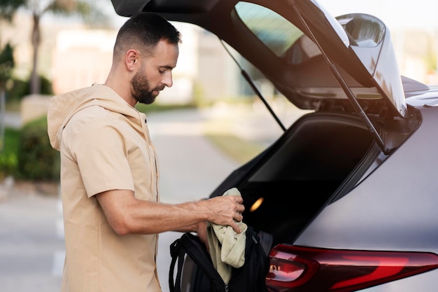 Knappe Latijns-man laadt tas in auto kofferbak. Bestuurder die roadtrip, transportconcept plant