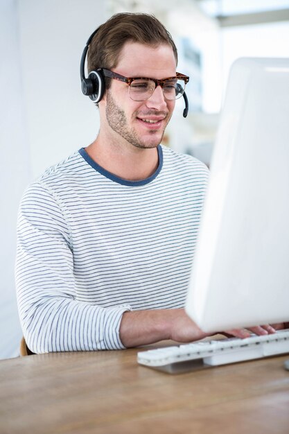 Knappe man aan het werk op computer met hoofdtelefoon in een heldere kantoor