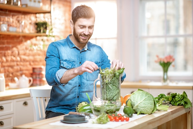 Knappe man die blender vult met groene rauwkost, vegetarische smoothie maakt in de keuken thuis