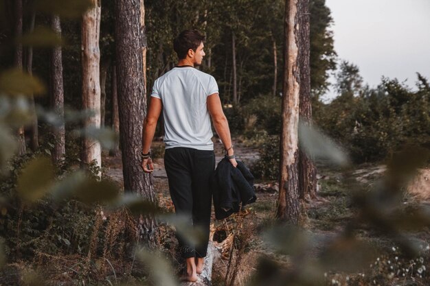 Knappe man die buiten in het bos poseert, staat blootsvoets op een boomstam met een geruit jasje