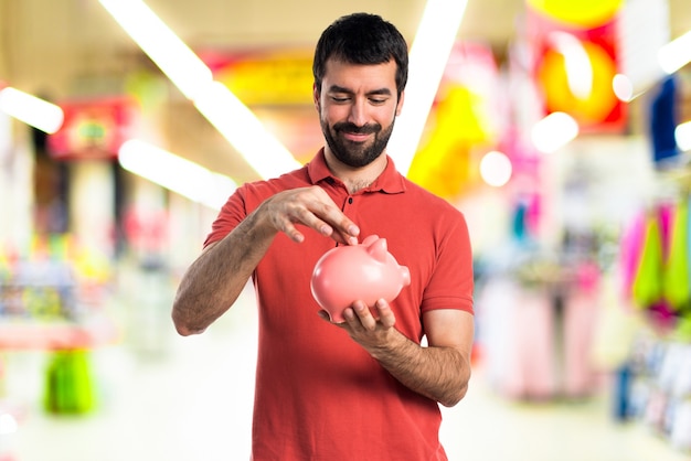 Knappe man die een piggybank op een ongerichte achtergrond houdt