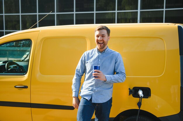 Knappe man die koffie drinkt tijdens het opladen van een elektrische auto