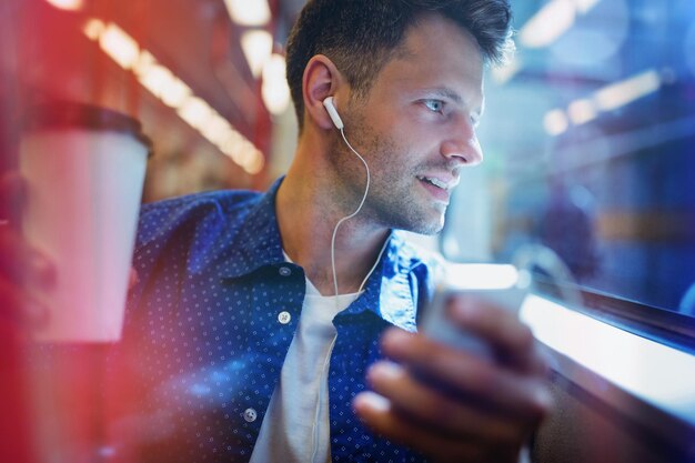 Knappe man die muziek luistert op mobiele telefoon terwijl hij koffie vasthoudt