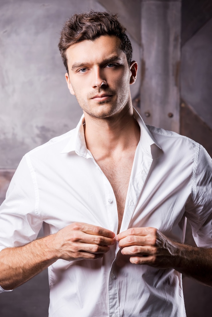 Foto knappe man die overhemd dichtknoopt. knappe jonge man die zijn witte overhemd dichtknoopt en naar de camera kijkt