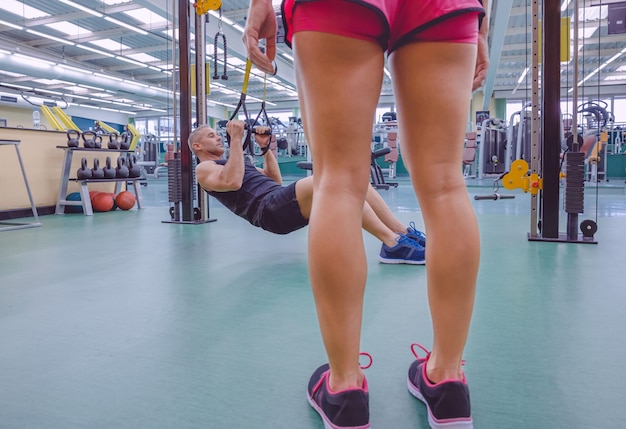 Knappe man doet harde schorsing training met fitness bandjes en vrouwelijke benen op de voorgrond.