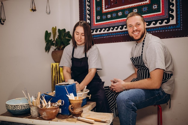 Knappe man en gelukkige vrouw paar verliefd bezig met pottenbakkerswiel terwijl man en vrouw in de kraft creatieve studio in de pottenbakkerij de winkel van het jonge familiebedrijf de pot uit klei beeldhouwt