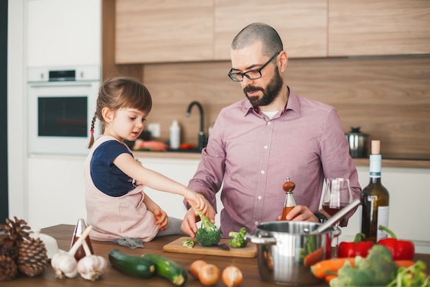 Knappe man en zijn schattige dochtertje koken samen groente stoofpot in de keuken. Gezond en vegetarisch voedselconcept.