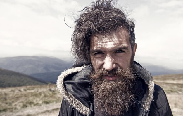 Knappe man hipster met baard en snor portret op de bergtop tegen blauwe mistige bewolkte hemel