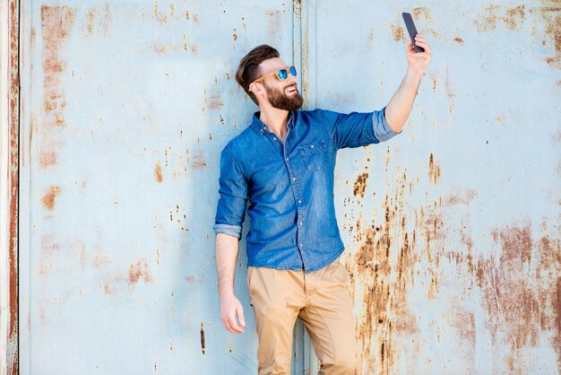 Knappe man in blauw t-shirt met telefoon op de oude roestige muurachtergrond