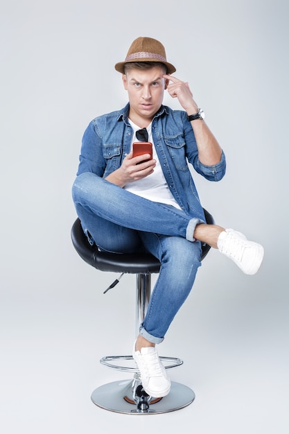 Knappe man in denim zit op stoel met telefoon