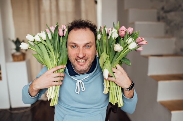 Knappe man in een sweatshirt glimlacht en houdt een boeket tulpen in zijn handen