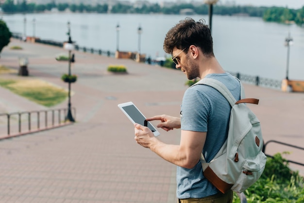 Knappe man in glazen met rugzak met behulp van digitale tablet