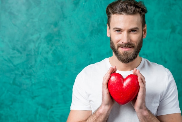 Foto knappe man in het witte t-shirt met rood hart op de geschilderde groene muur achtergrond. valentijnsdag concept