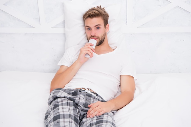 Knappe man in pyjama met afstandsbediening man televisie kijken in slaapkamer luie zondag thuis kijken ochtendshow man kijken tv kanaal veranderen door afstandsbediening in bed rusten in bed thuis