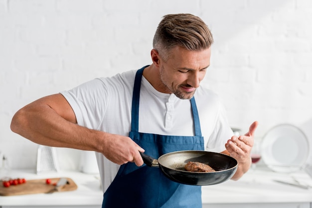 Knappe man in schort die gekookte steak ruikt