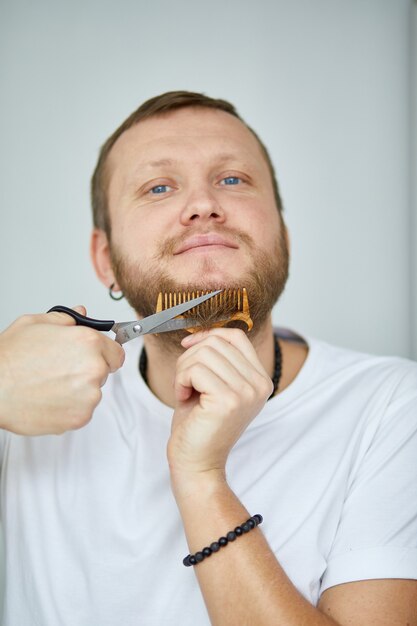 Knappe man in witte t-shirts die baard knippen, snor persoonlijk zelf