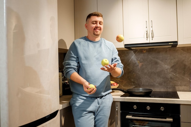 Knappe man jongleren met appels in moderne keuken