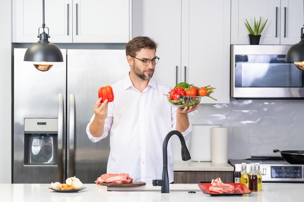 Knappe man koken salade in keuken man leunend op keuken met groenten portret van casual man