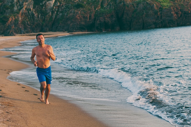 Knappe man loopt op het strand van de zonsondergang