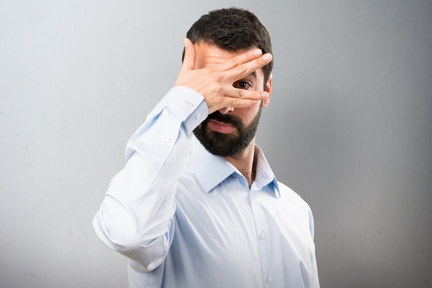 Knappe man met baard die zijn ogen op getextureerde achtergrond bedekt