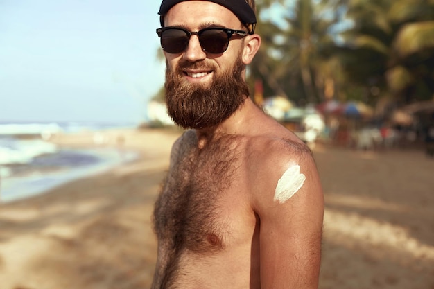 Knappe man met baard in zonnebril zonnebaden met zonnebrandcrème lichaam in de zomer