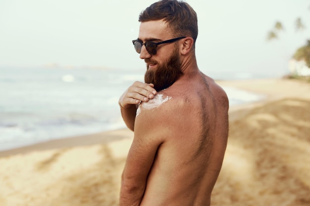 Knappe man met baard in zonnebril zonnebaden met zonnebrandcrème lichaam in de zomer