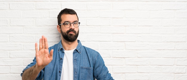 Knappe man met baard over witte bakstenen muur stop gebaar maken