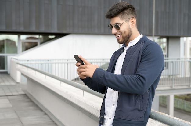 Knappe man met behulp van mobiele telefoon app sms'en buiten kantoor in stedelijke stad met wolkenkrabbers gebouwd...