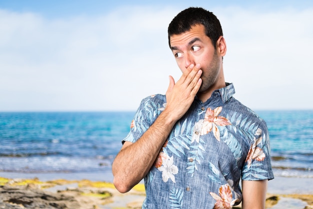 Knappe man met bloem shirt bedekt zijn mond op het strand