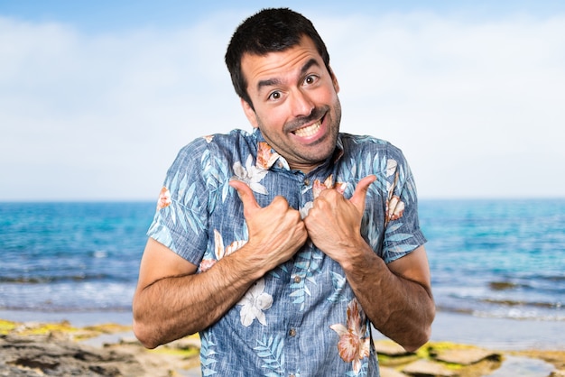 Knappe man met bloem shirt met duim omhoog op het strand