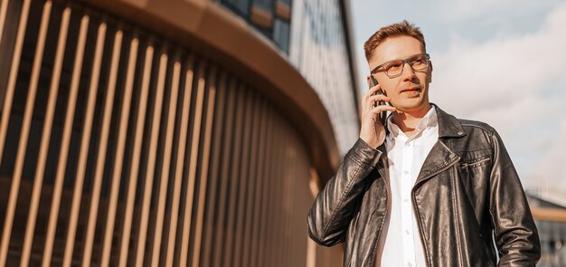 Knappe man met bril met een smartphone op straat van een grote stad. Zakenman praten aan de telefoon op stedelijke achtergrond