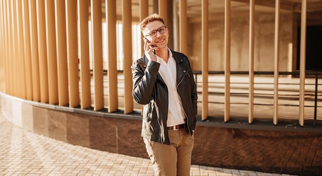 Knappe man met bril met een smartphone op straat van een grote stad Zakenman praten aan de telefoon op stedelijke achtergrond