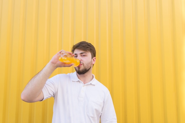 Knappe man met een baard drinkt sap uit een fles op een gele muur.