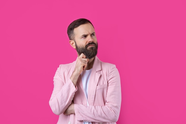 Knappe man met een baard in een roze jas denkt over een geïsoleerde rode achtergrond