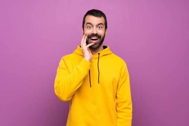 Knappe man met gele sweater met verrassing en geschokte gelaatsuitdrukking