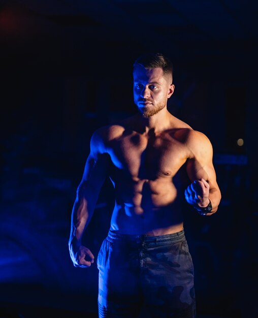 Knappe man met grote spieren, die zich voordeed op de camera in de sportschool, blauw licht.