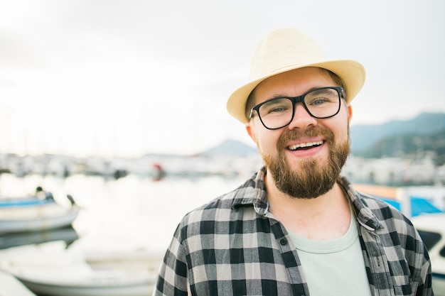Knappe man met hoed en bril in de buurt van jachthaven met jachten portret van lachende man met zeehavenachtergrond met kopieerruimte