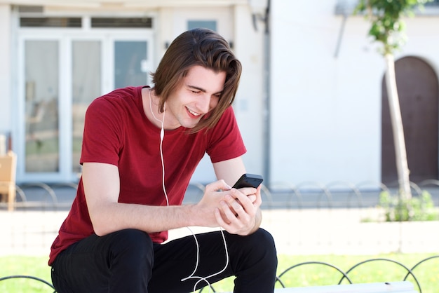 Knappe man met hoofdtelefoon buiten met slimme telefoon