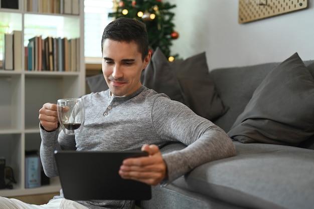 Knappe man met koffiekopje en surfen op internet met digitale tablet thuis.
