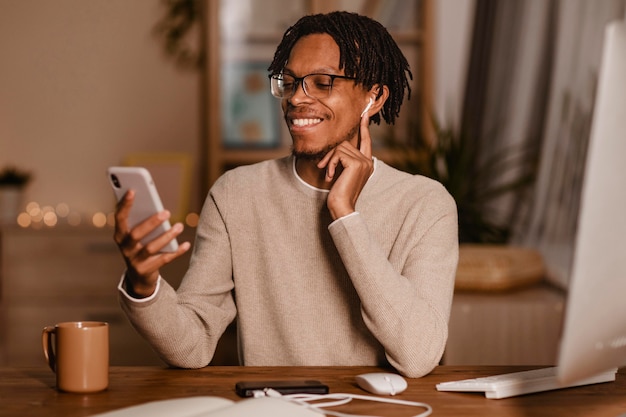 Knappe man met zijn smartphone thuis met oordopjes