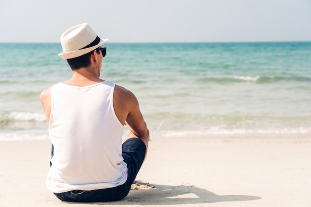 Knappe man met zonnebril en strand hoed ontspannen op het strand