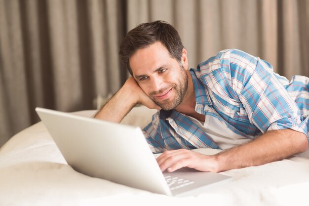 Knappe man ontspannen op zijn bed met laptop