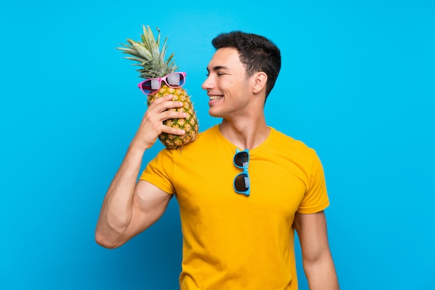 Knappe man over blauwe achtergrond met een ananas met sunglasse