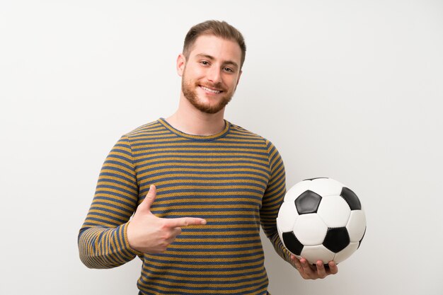 Knappe man over geïsoleerde witte muur met een voetbal