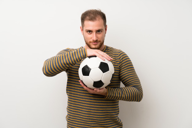 Knappe man over geïsoleerde witte muur met een voetbal