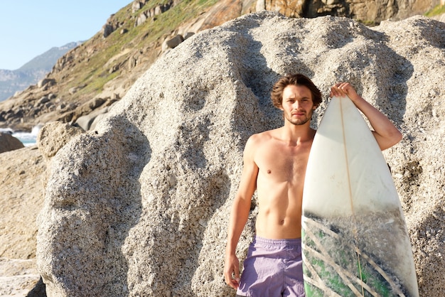 Knappe man poseren met surfboard op het strand