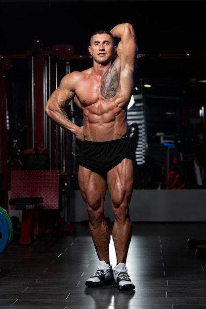 Knappe man staat sterk in de sportschool en buigt spieren Gespierde atletische bodybuilder Fitness Model poseren na oefeningen